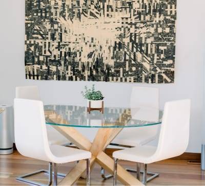 Salón con un cuadro abstracto y una mesa redonda de cristal con una pequeña planta y 4 sillas blancas modernas alrededor